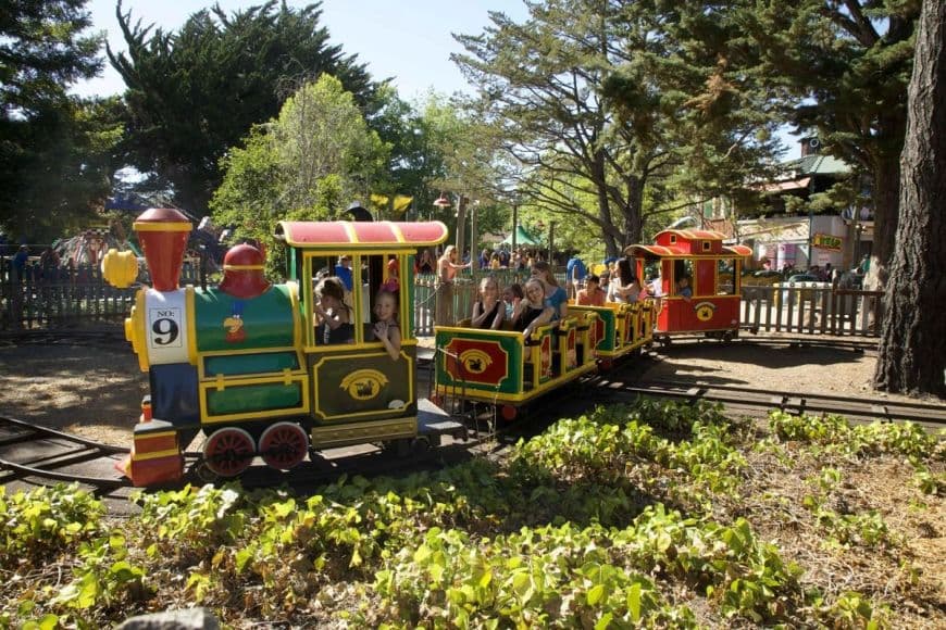 Foghorn's Seaport Railway in motion at Six Flags Discovery Kingdom, with guests smiling for the camera.