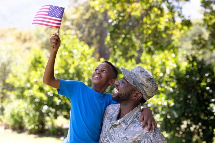 Father wearing military uniform while holding his son who is waving the American Flag