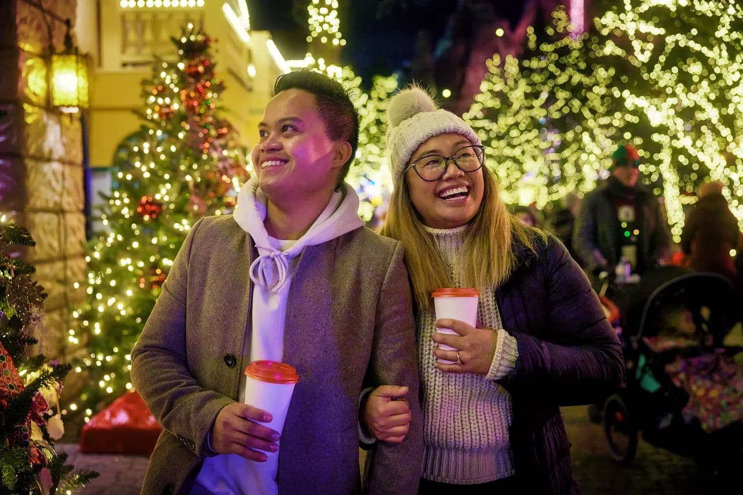 Couple walking together looking at holiday lights while holding cups and smiling