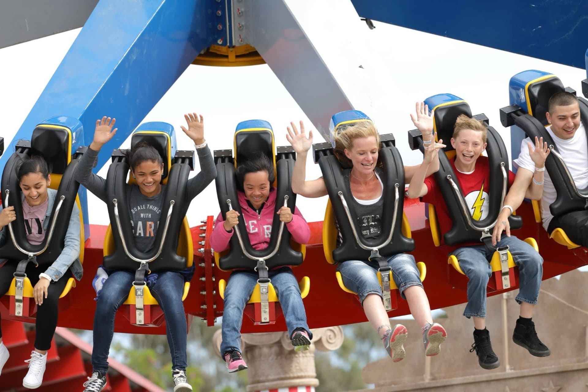 A close-up of young thrill seekers with their hands in the air as they scream riding the WONDER WOMAN Lasso of Truth ride.